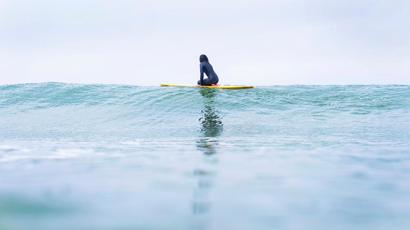 Women on surfboard looking out at ocean.